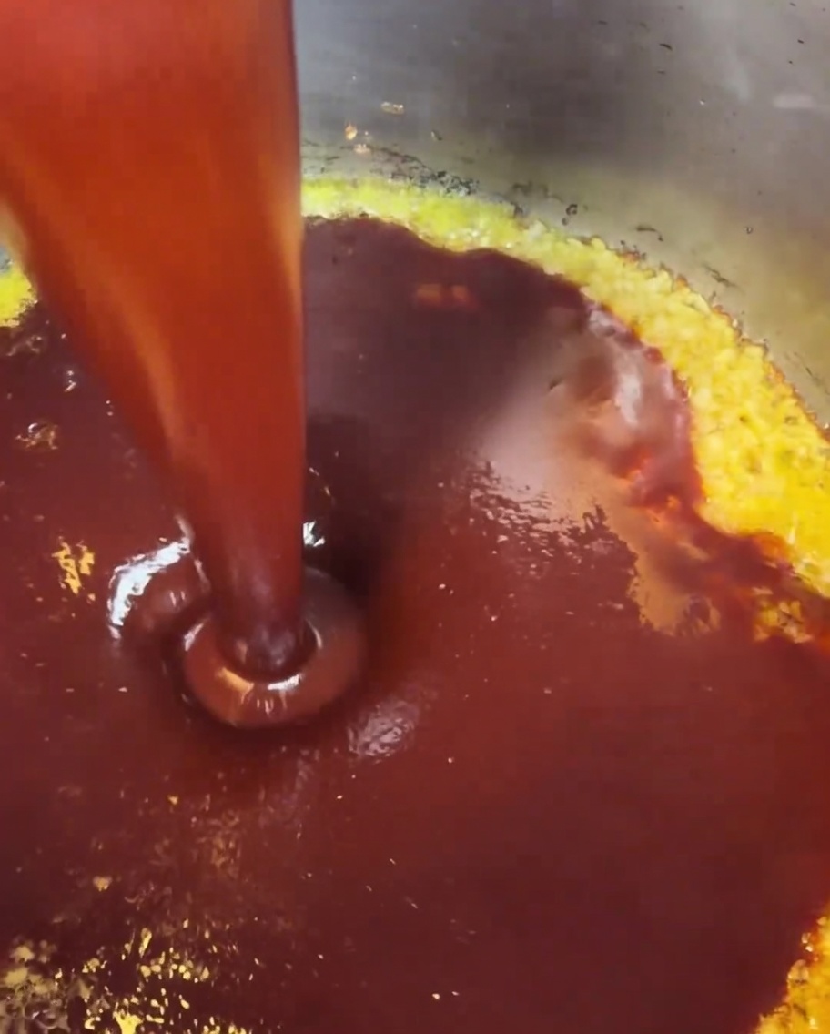 La salsa rossa mescolata versata nella pentola dove aglio e burro stanno già sobbollendo.