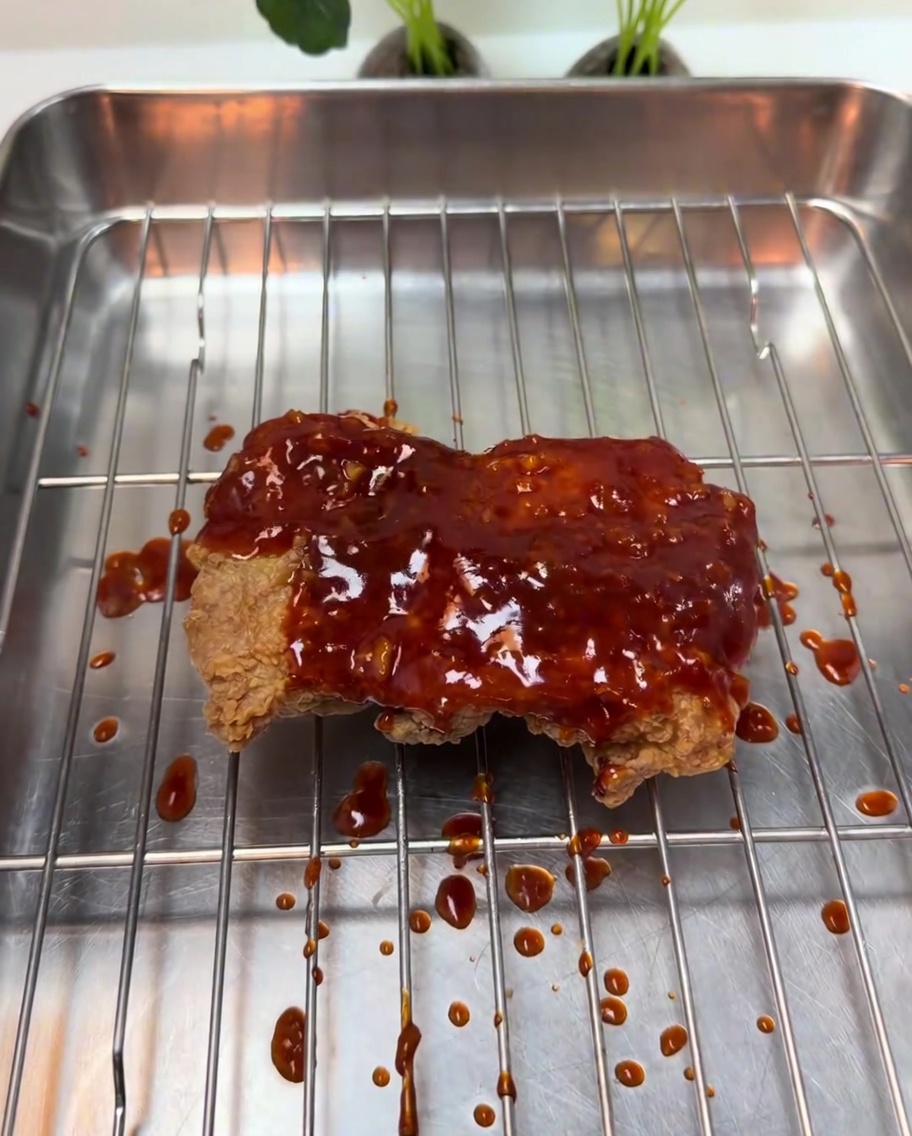 Una densa glassa rossa al peperoncino versata sul pollo fritto croccante.