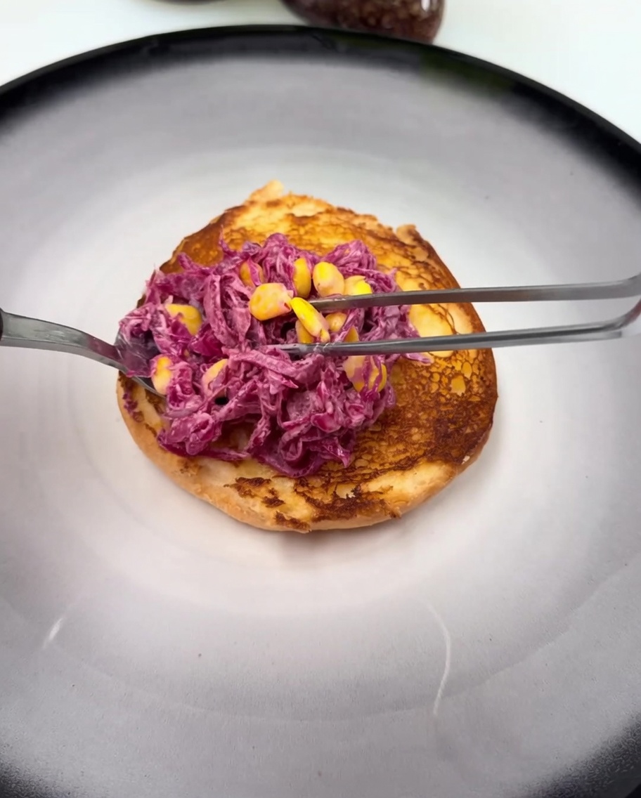 Il pane da burger tostato alla base, guarnito con uno strato di salsa e una porzione di insalata di cavolo viola e mais.