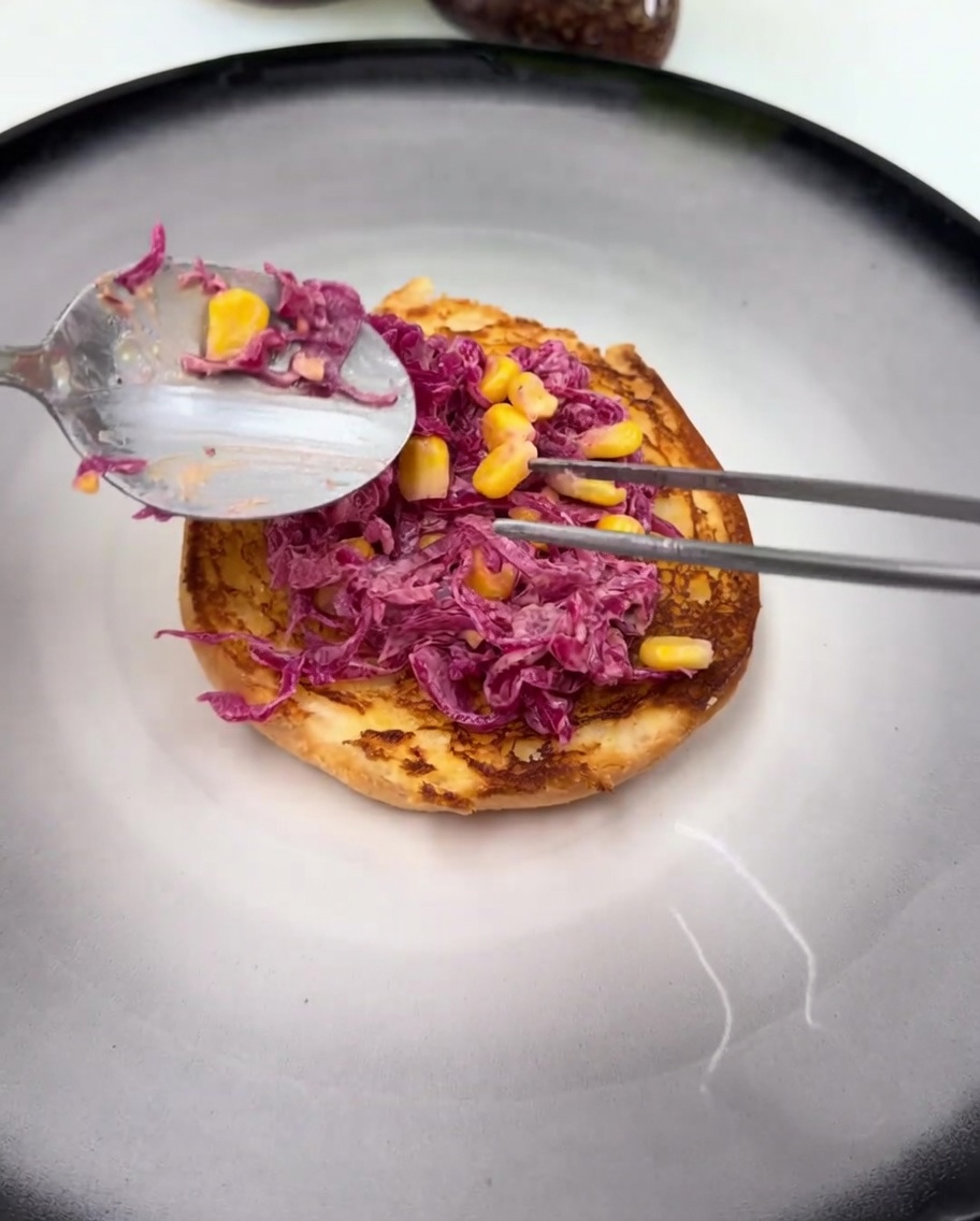Una coscia di pollo fritta e glassata che riposa sopra linsalata di cavolo sul pane da burger.