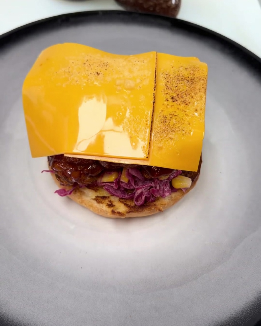 Una fetta di formaggio cheddar che si scioglie sul pollo fritto glassato, con visibili segni di doratura dal cannello.