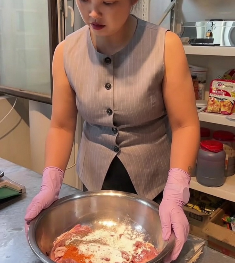 Pezzi di pollo crudo mescolati con spezie e marinatura in unampia ciotola in acciaio inossidabile.