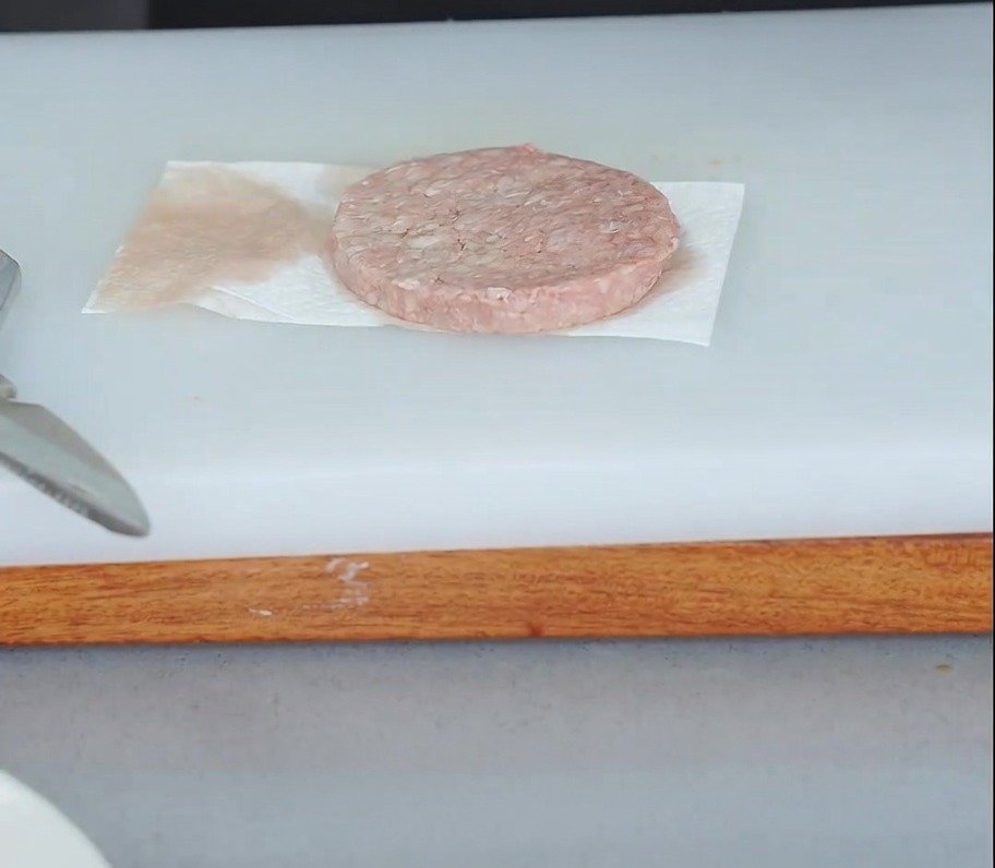 Un hamburger crudo su carta assorbente mentre viene tamponato per rimuovere lumidità in eccesso.