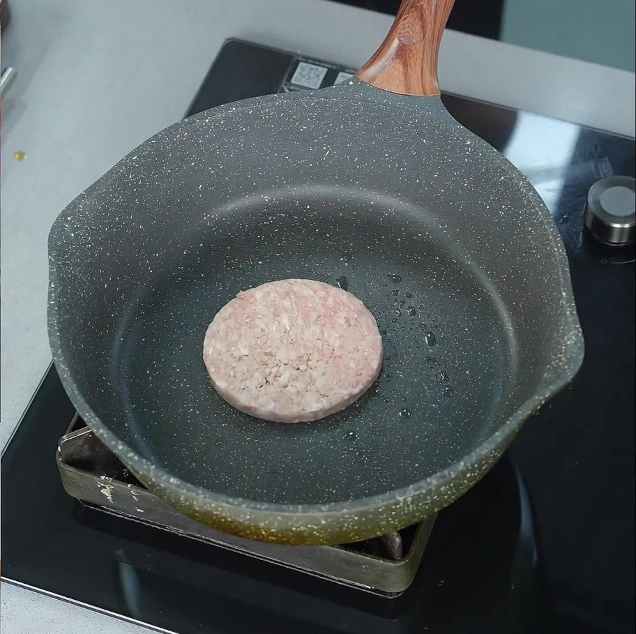 Un hamburger di manzo che sfrigola in una padella leggermente oliata.