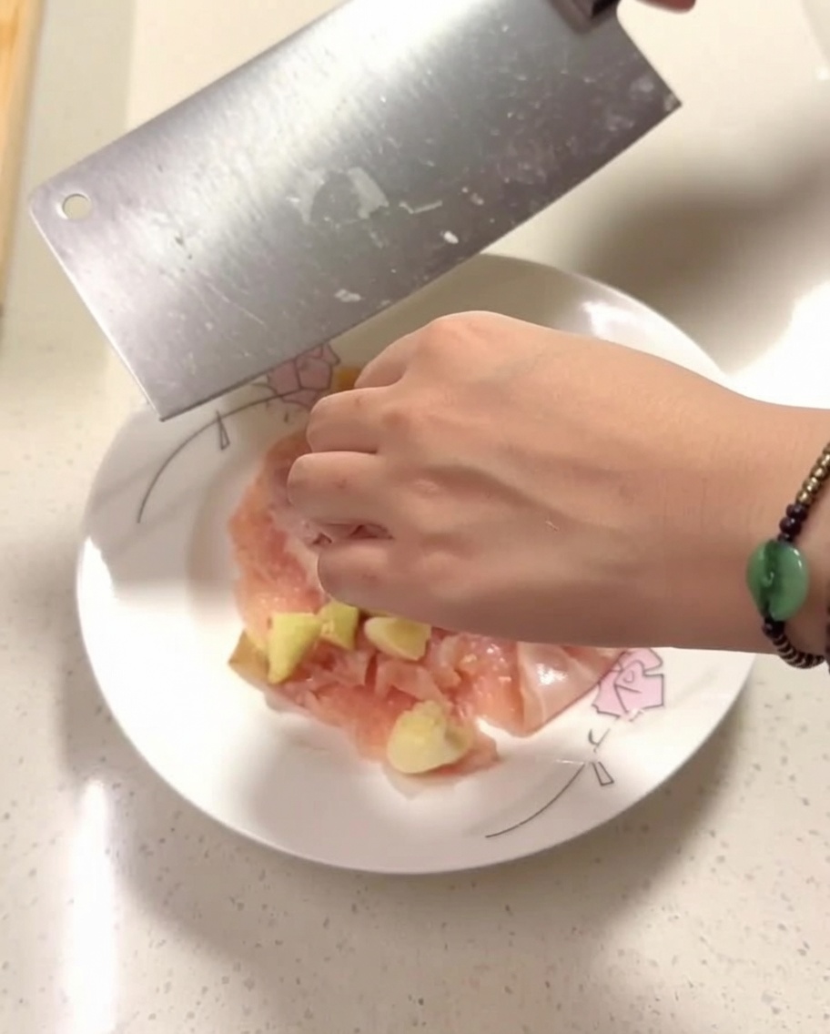 Pezzi di pollo crudo su un piatto conditi con zenzero, aglio e spezie.