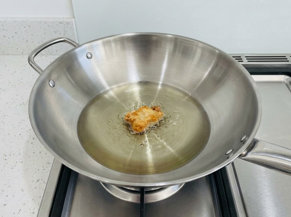 Un pezzo di pollo impanato fritto in un wok pieno di olio caldo.
