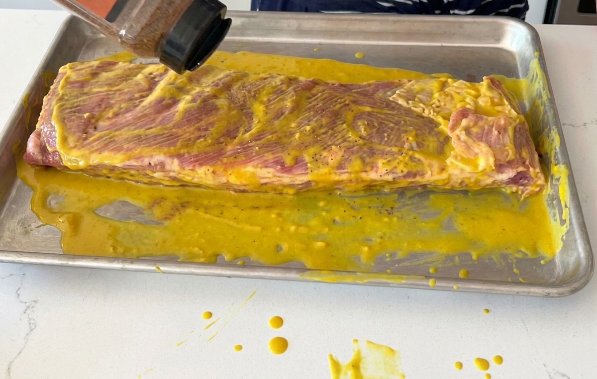 Spolverata di dry rub BBQ sopra una baffa di costine di maiale ricoperta di senape gialla.