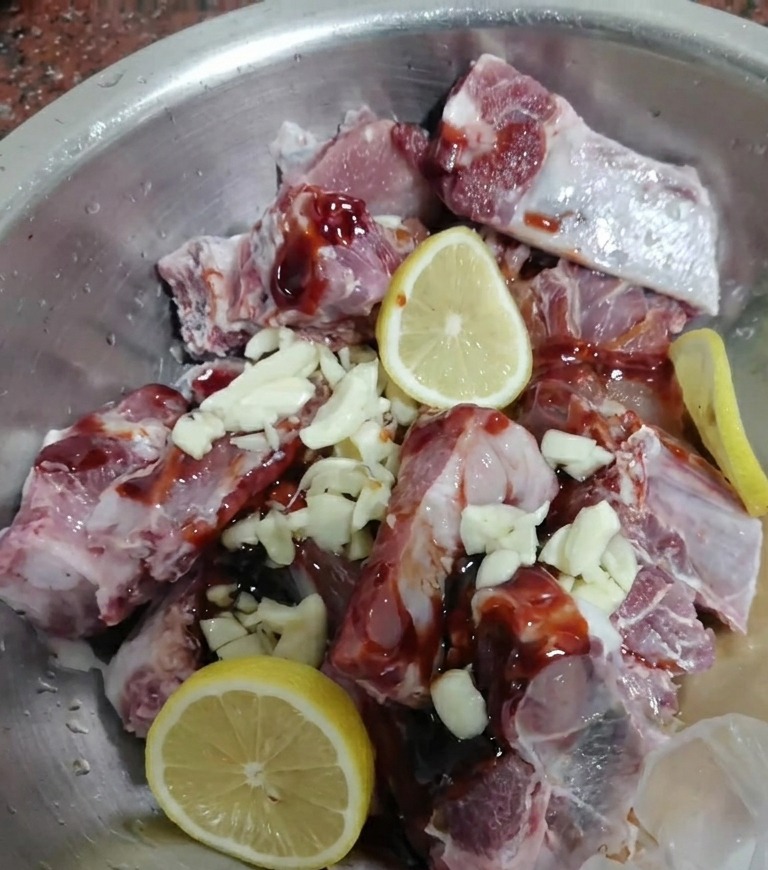Costolette di maiale crude mescolate con marinata scura, aglio e fette di limone.