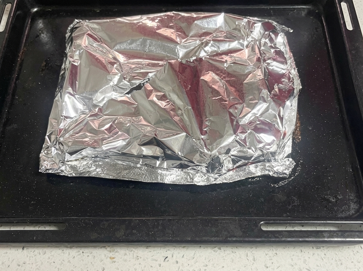 Un coltello taglia lo strato superiore di alluminio per rivelare le costine cotte e fumanti.