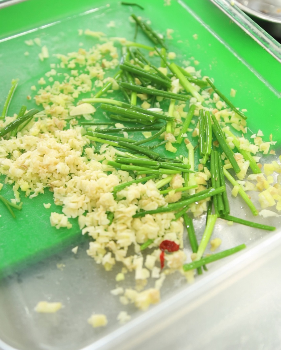 Un contenitore con aglio tritato fresco, erba cipollina tritata verde brillante e una generosa quantità di pasta di peperoncino coreano rossa scura.