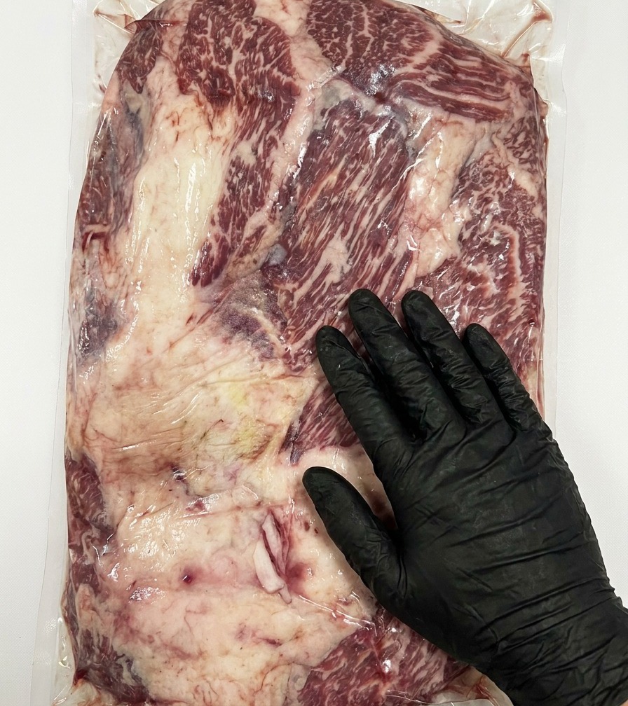 Primo piano di un coltello che rimuove leccesso di grasso dalla superficie di un brisket di Wagyu crudo.