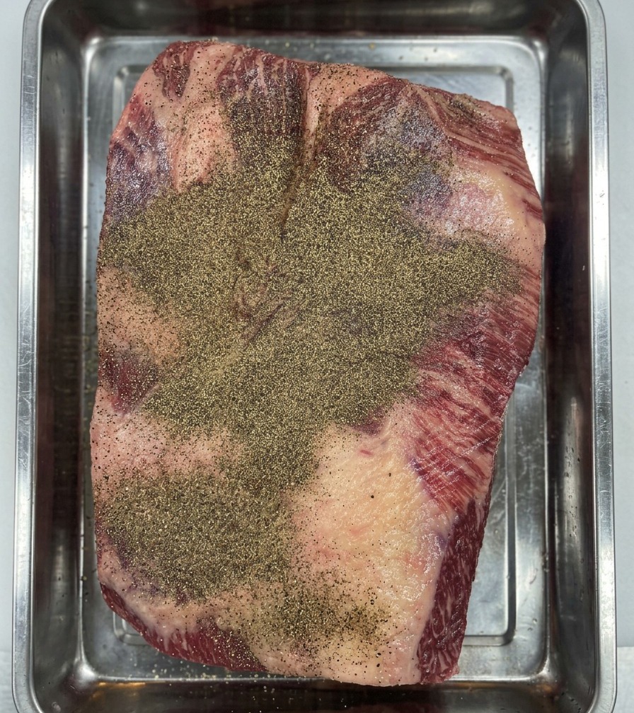 Mani guantate che premono il pepe nella carne per creare uno strato uniforme.