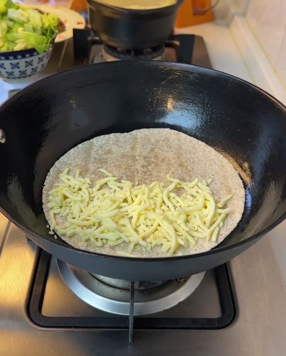 Lattuga finemente tritata aggiunta sopra il formaggio fuso su una tortilla.