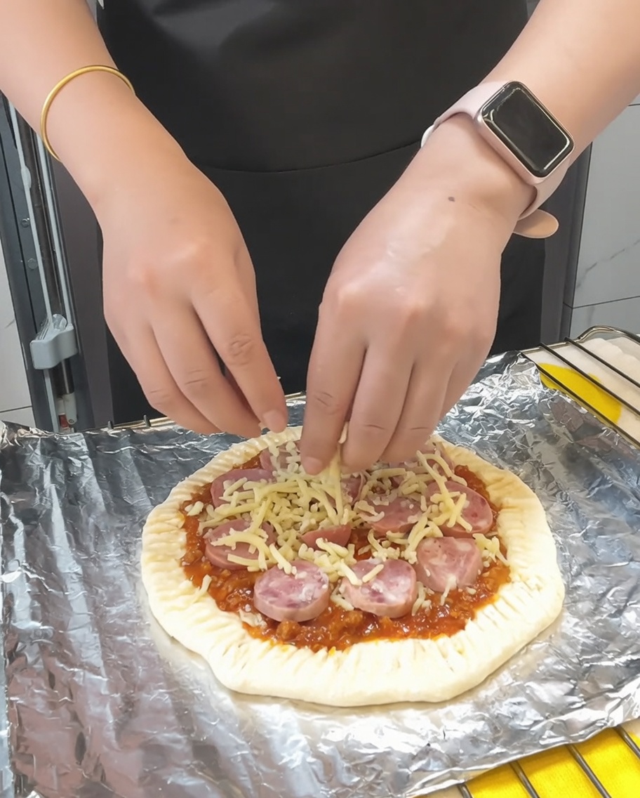Unultima manciata di mozzarella sparsa sulla pizza, seguita da una leggera spolverata di prezzemolo essiccato.
