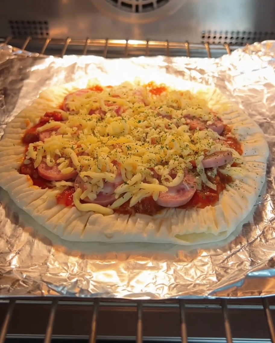 Una pizza di pancake alle scalogne appena sfornata con formaggio fuso e fette di salsiccia, posizionata su una griglia in forno.