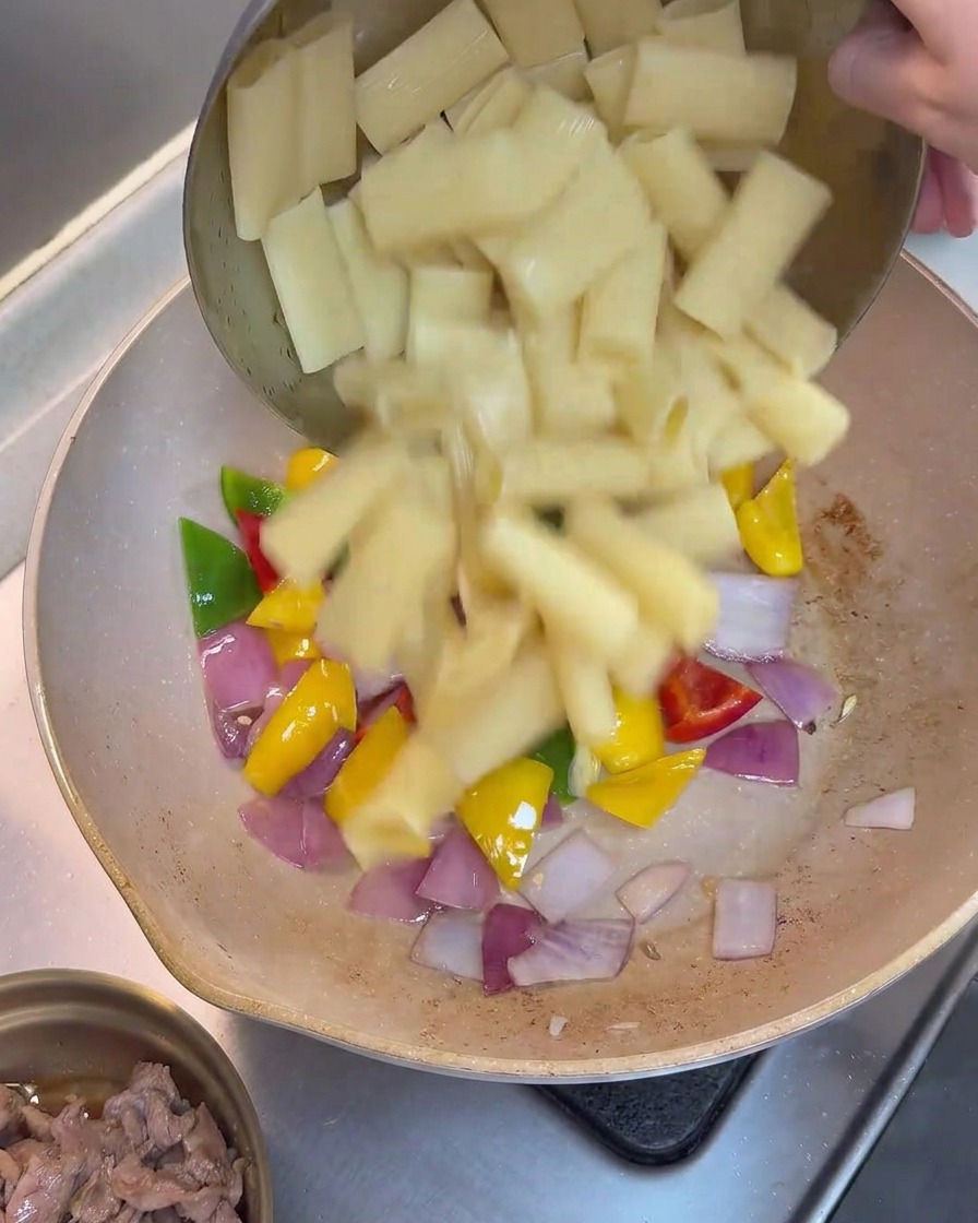 Rigatoni cotti aggiunti alla padella con peperoni e cipolle saltati.