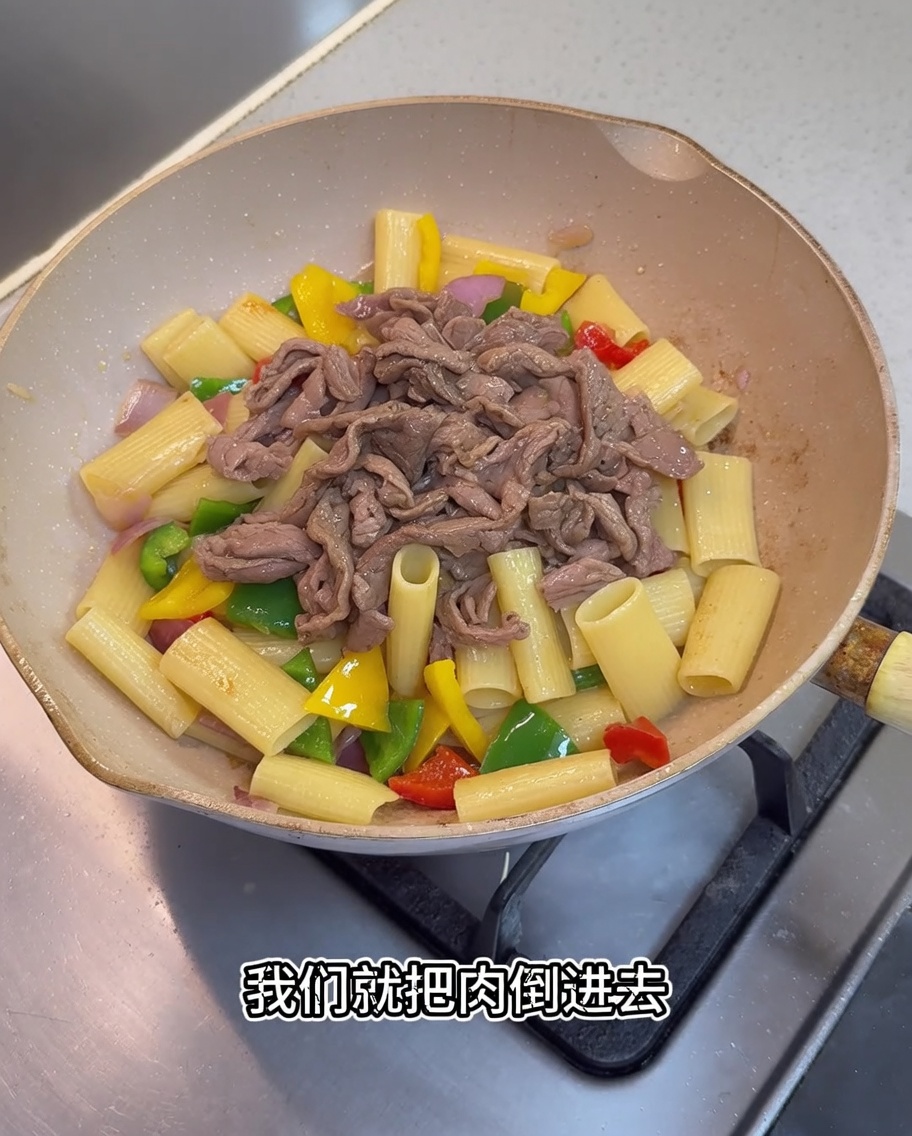 Pezzi di maiale cotto e una salsa scura versata nella padella contenente i rigatoni e le verdure.