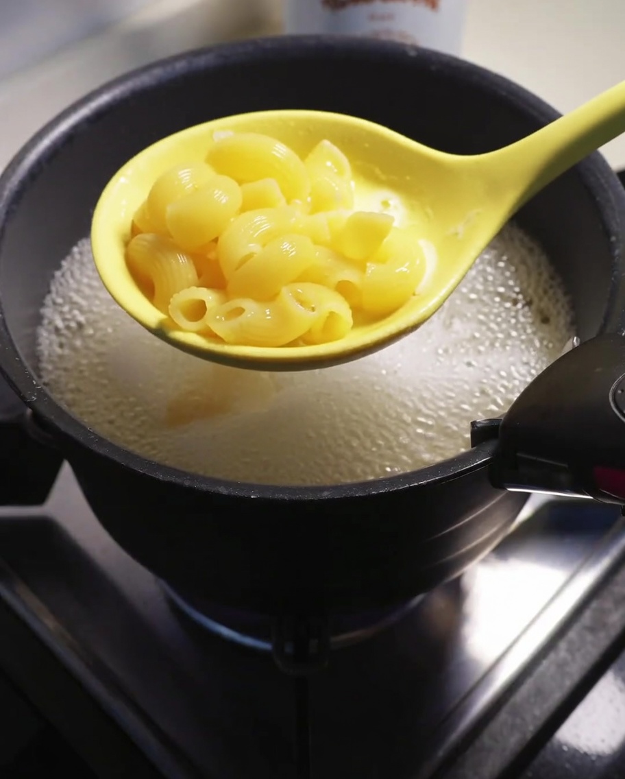 Maccheroni cotti sollevati dallacqua bollente con una schiumarola gialla.