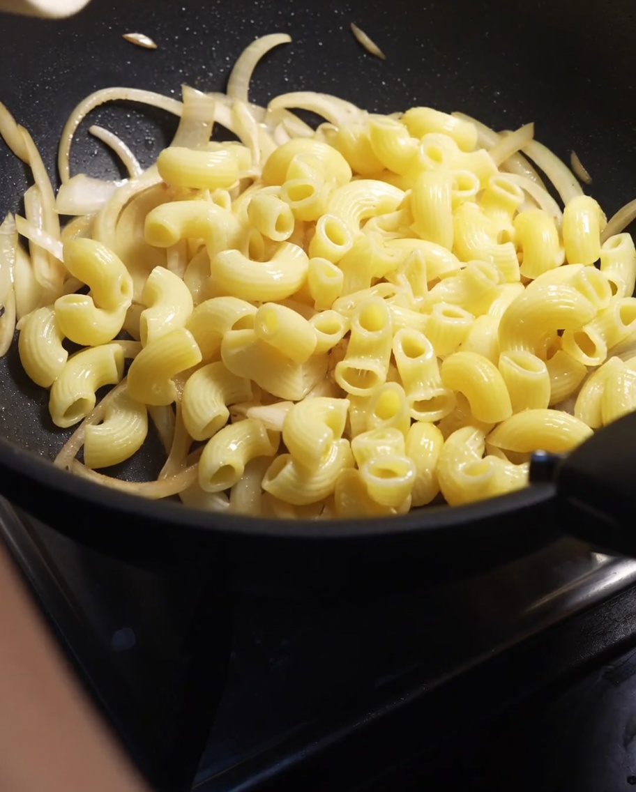 Maccheroni versati in una padella con cipolle affettate ammorbidite.