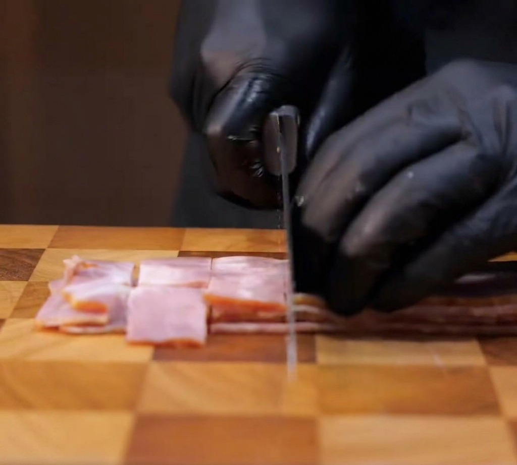 Fette di pancetta tagliate a cubetti su un tagliere di legno.