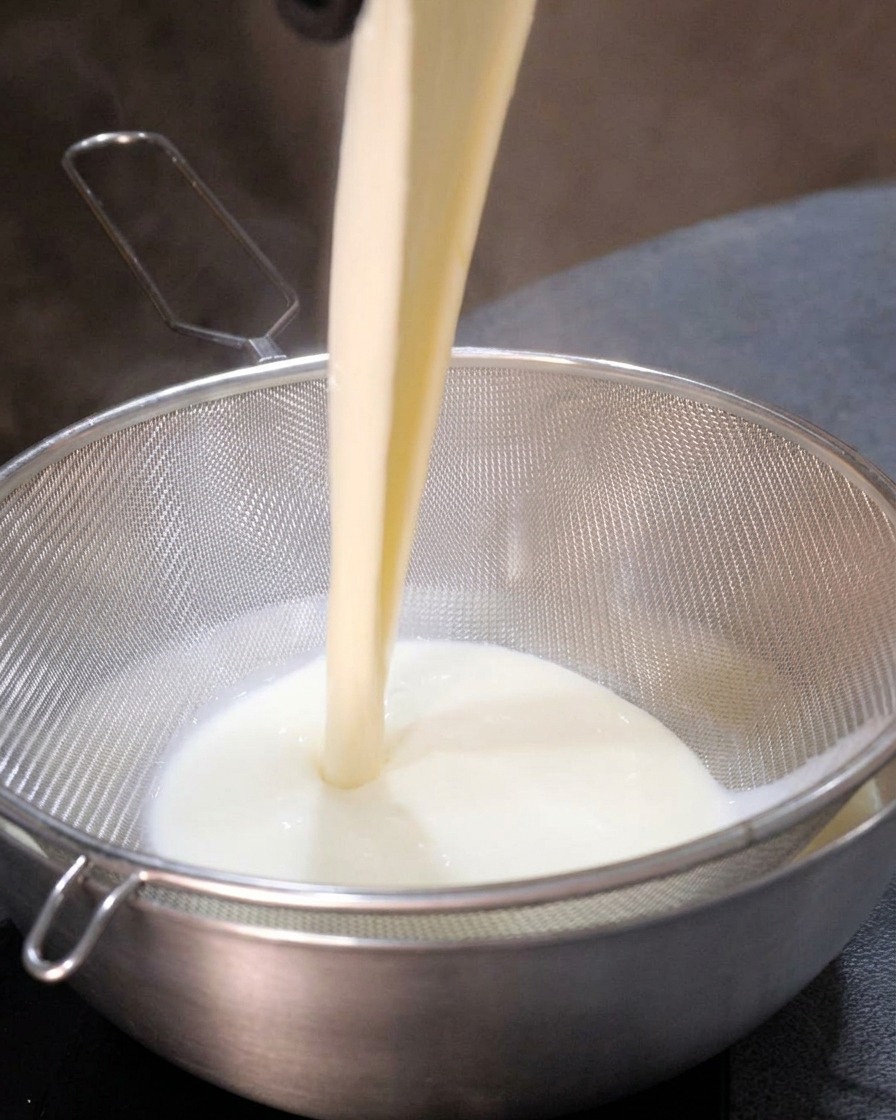 La base cremosa della zuppa versata attraverso un setaccio di metallo, risultando in un liquido liscio nella ciotola sottostante.