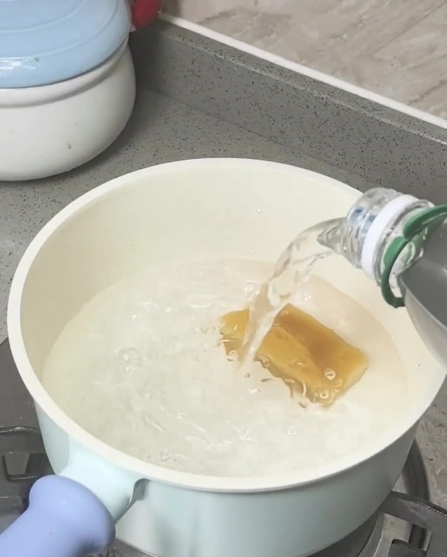 Blocco di zucchero di canna che si scioglie in acqua bollente in una pentola chiara.