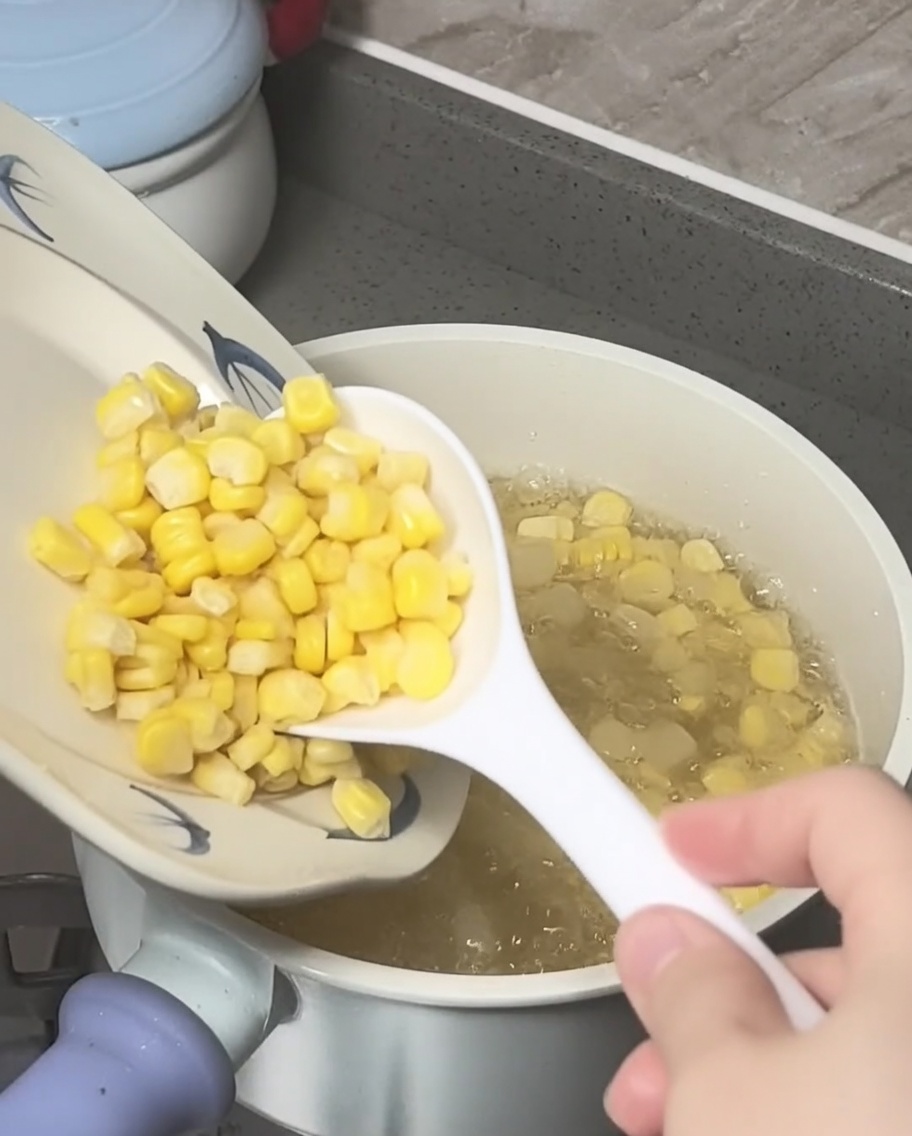 Chicchi di mais e castagne dacqua schiacciate aggiunti in una pentola di acqua zuccherata in ebollizione.