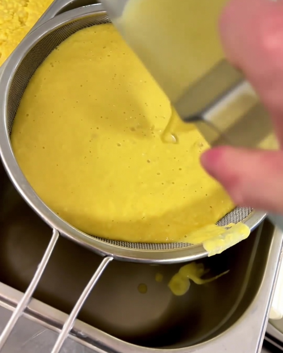 Zuppa di mais versata attraverso un colino a maglie fini in un contenitore.