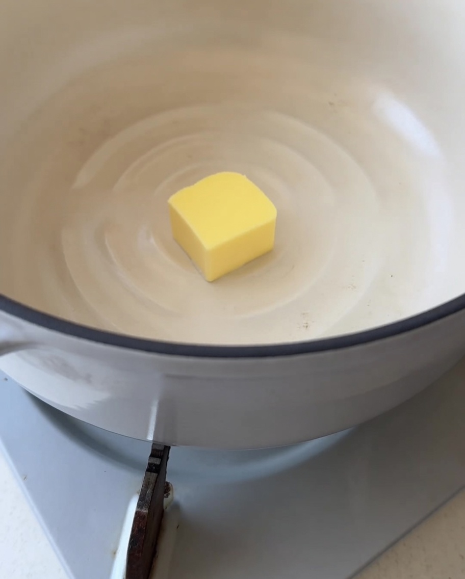 Primo piano di un cubetto di burro giallo che inizia a sciogliersi in una pentola bianca pulita.