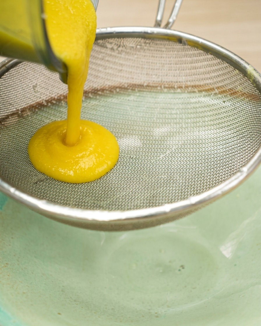 Una densa purea di mais giallo viene filtrata attraverso un setaccio a maglie fini in acciaio inossidabile in una ciotola.