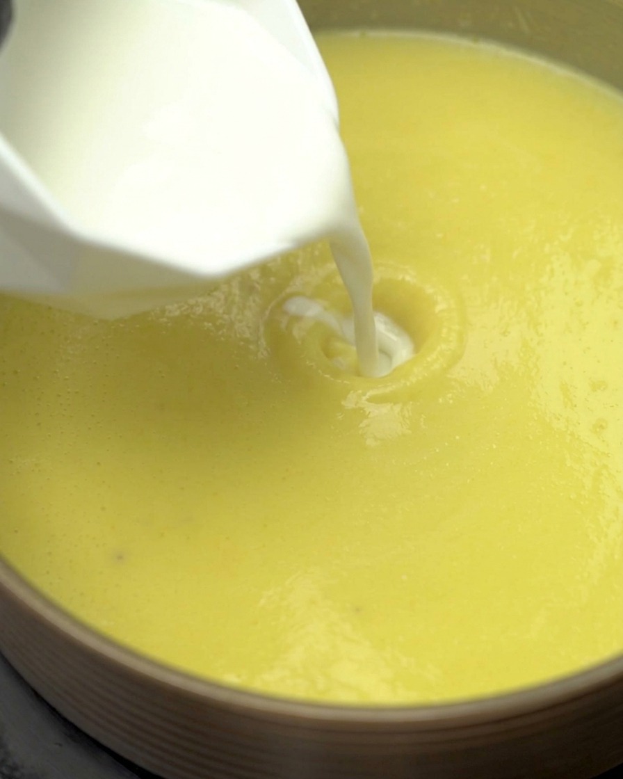 Latte e panna leggera vengono versati nella base della zuppa di mais che sobbolle in una pentola.