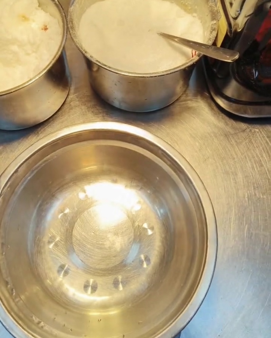 Molti piccoli contenitori di metallo pieni di vari condimenti granulari bianchi e liquidi su un tavolo di preparazione.
