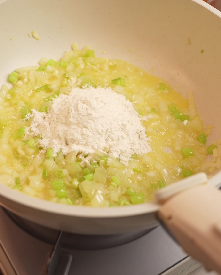 Farina mescolata al trito di cipolla e sedano in una padella.