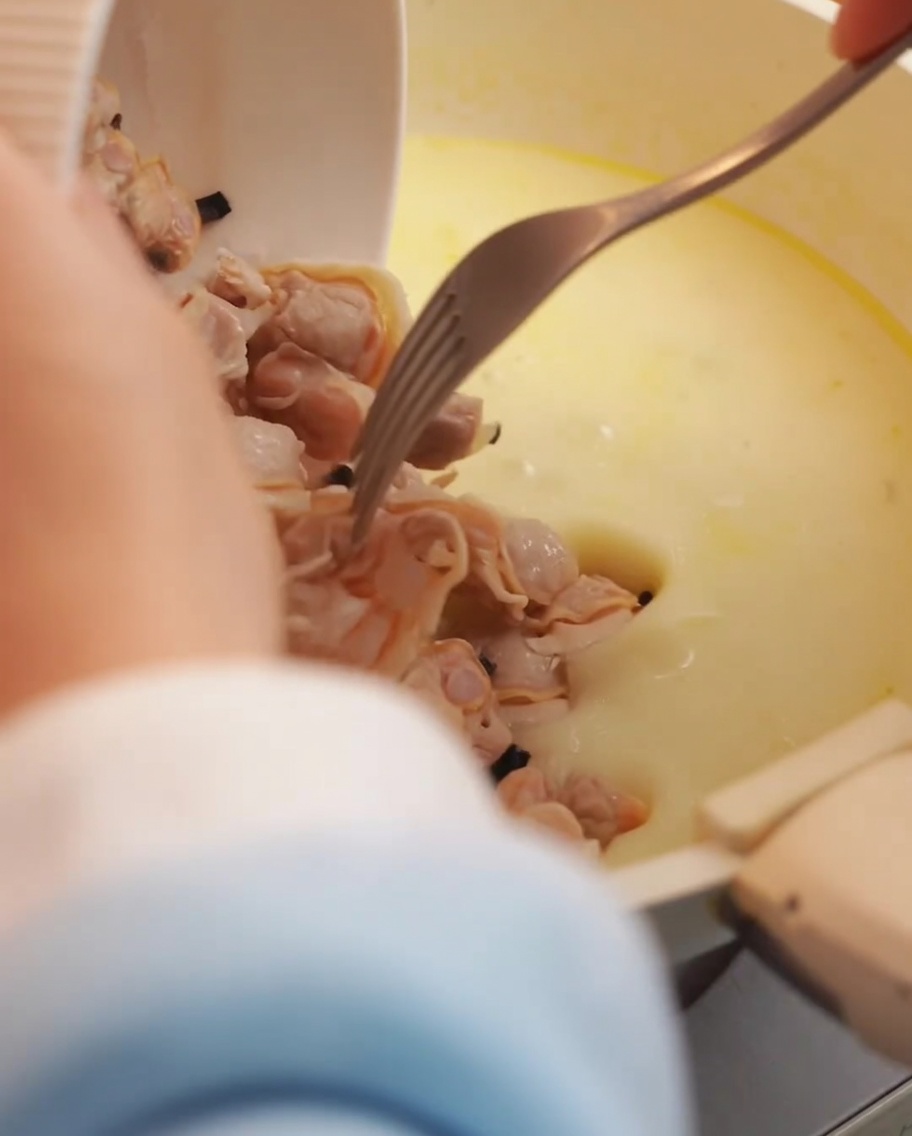 Polpa di vongole fresche e pancetta croccante aggiunte alla base cremosa della zuppa nella pentola.