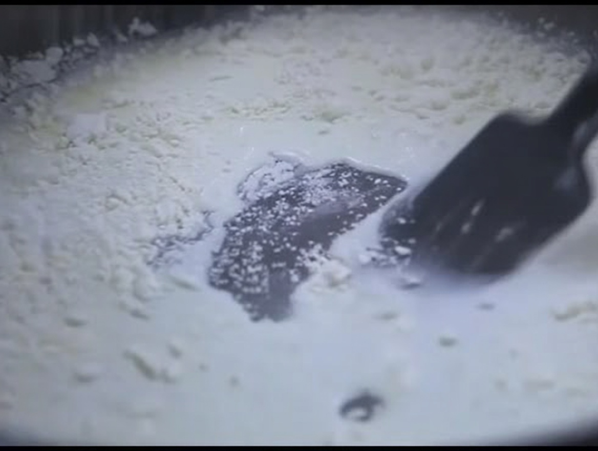 Una spatola in silicone nera che mescola un composto denso bianco di latte e farina in una padella.