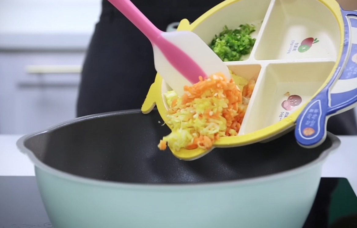 Carote, patate e sedano tritati versati da un piattino per bambini in una pentola.