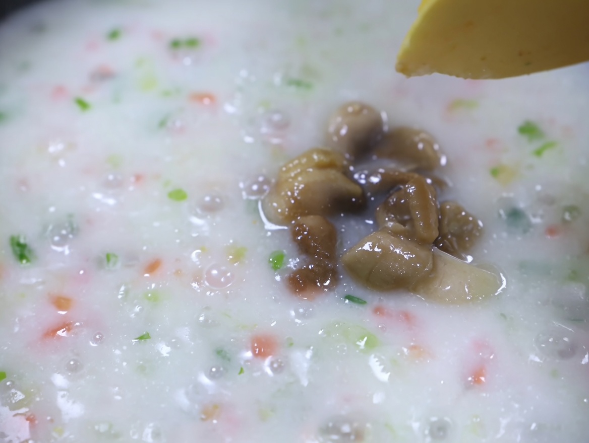 Polpa di vongole cotta aggiunta a una zuppa cremosa di verdure in ebollizione.