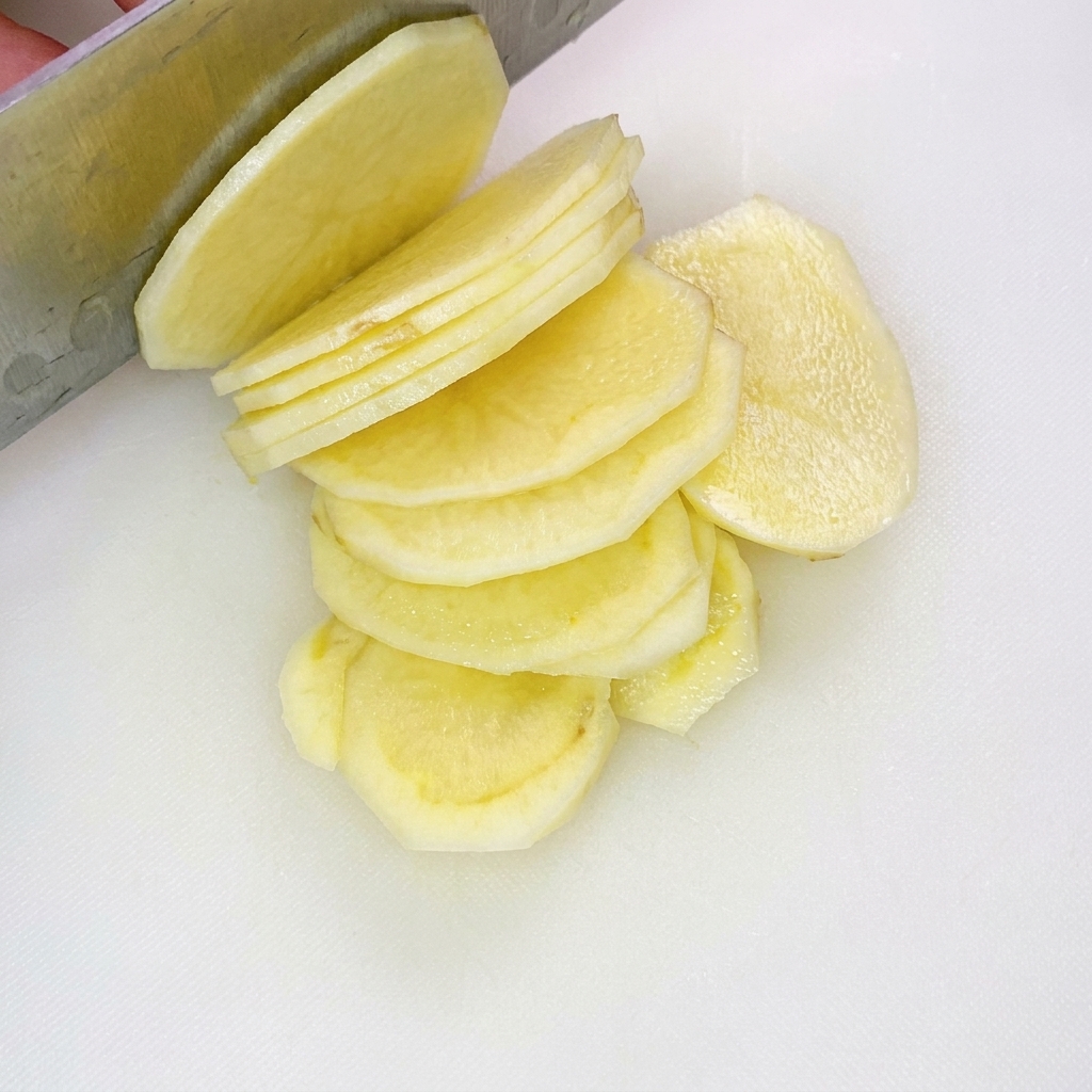 Listarelle di patate tagliate in modo uniforme e distribuite su un tagliere bianco.