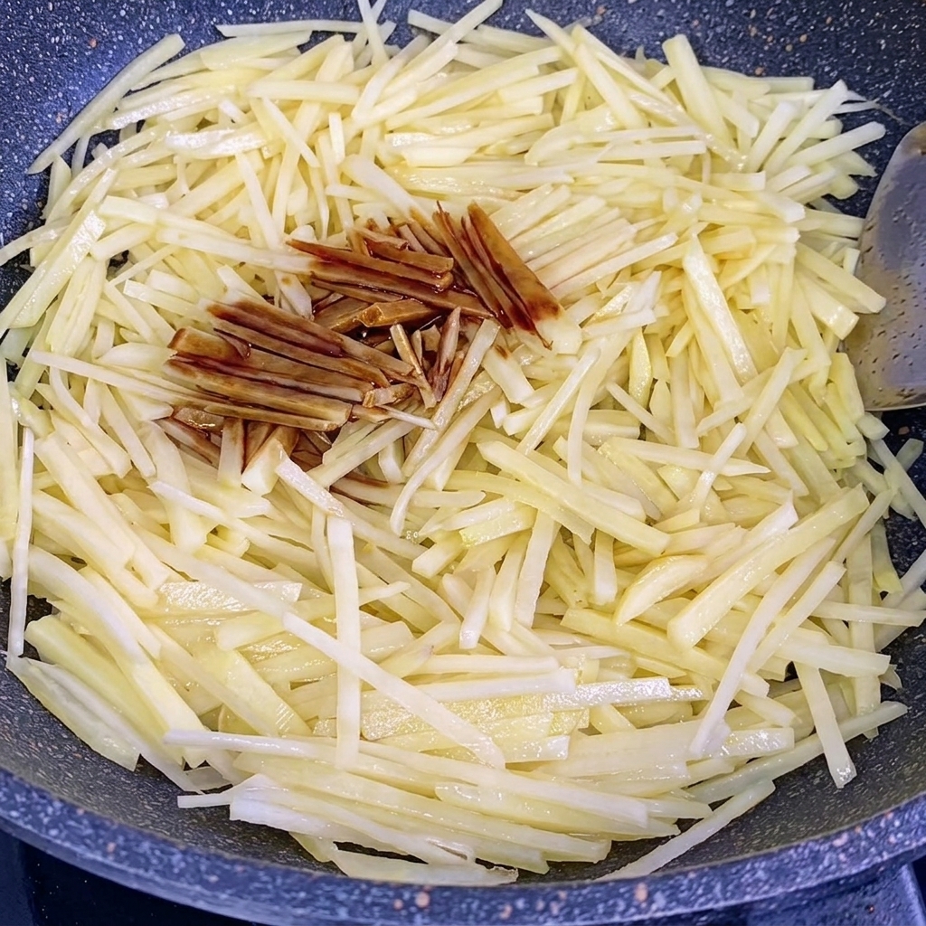 Salsa di soia e salsa di ostriche versate sulle patate saltate in un wok.