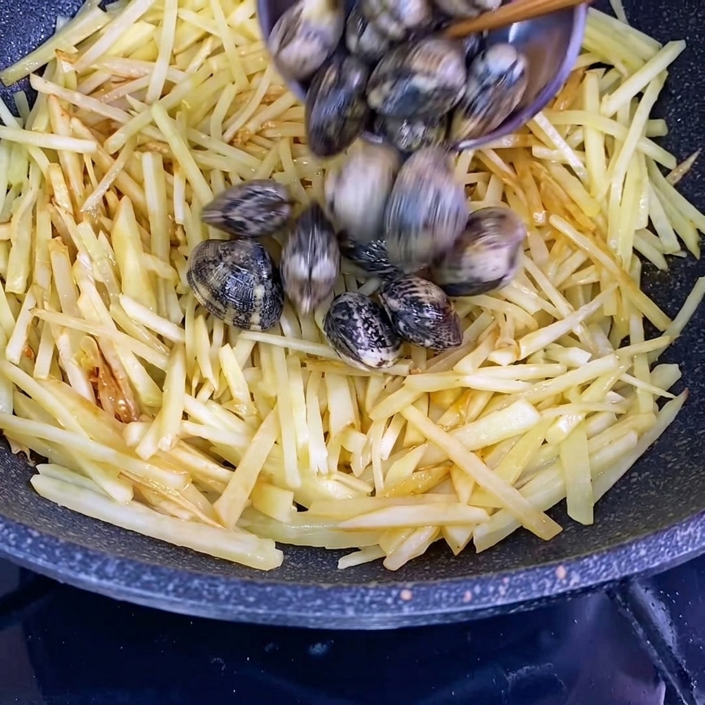 Vongole fresche con il guscio aggiunte al wok con le patate condite.