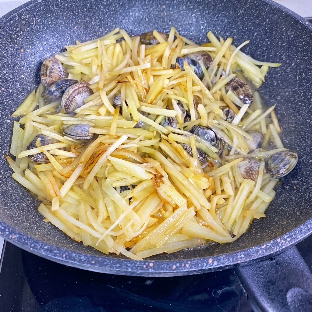 Acqua versata in un wok contenente patate saltate e vongole fresche.