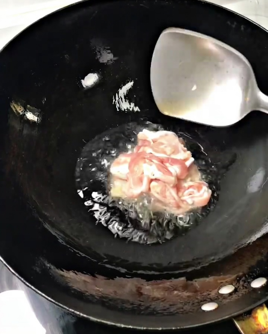 Sottili fettine di maiale sfrigolano in un wok caldo con olio, mescolate con una spatola di metallo.