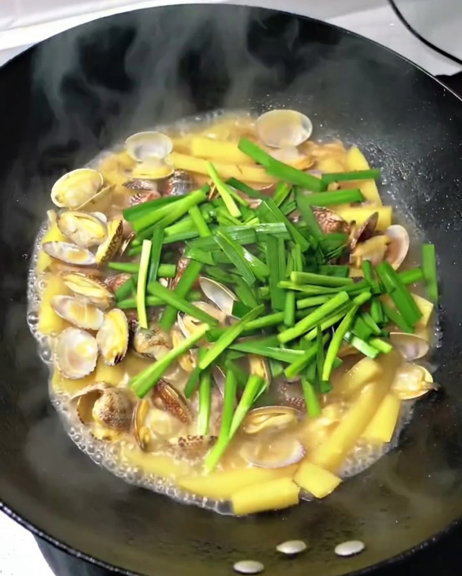 Erba cipollina cinese fresca tritata sparsa nel wok con vongole, patate e maiale.