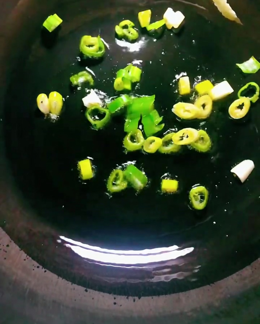 Cipollotti che soffriggono in olio caldo in un wok scuro.