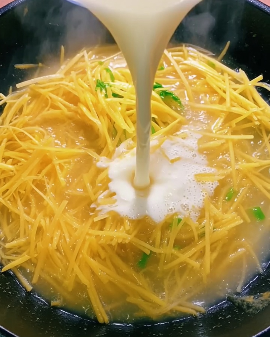 Liquido limpido versato da una ciotola in un wok contenente patate saltate.