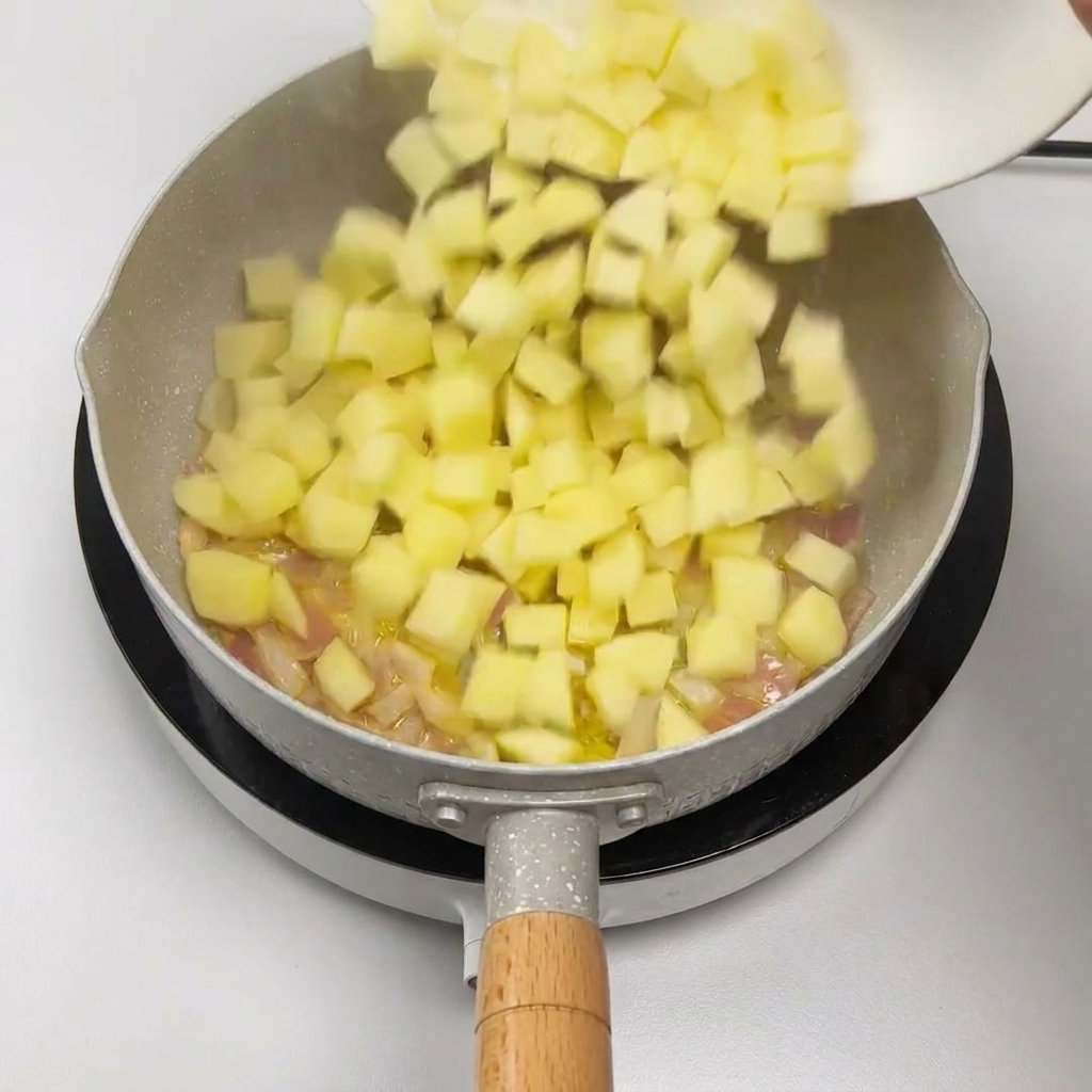 Cubetti di patate versati da un piatto bianco in padella con le cipolle soffritte.