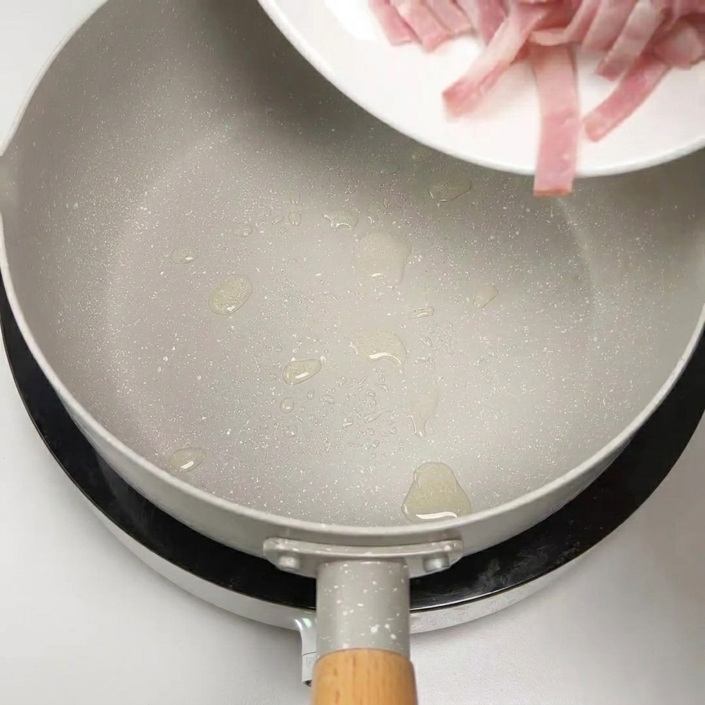 Strisce di bacon crudo aggiunte in una padella per essere rosolate.