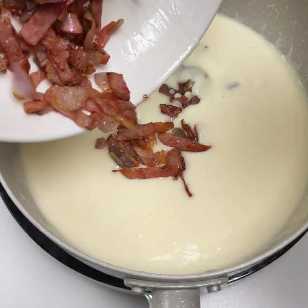 Bacon e cipolle rosolate versati da un piatto nella zuppa di patate cremosa.