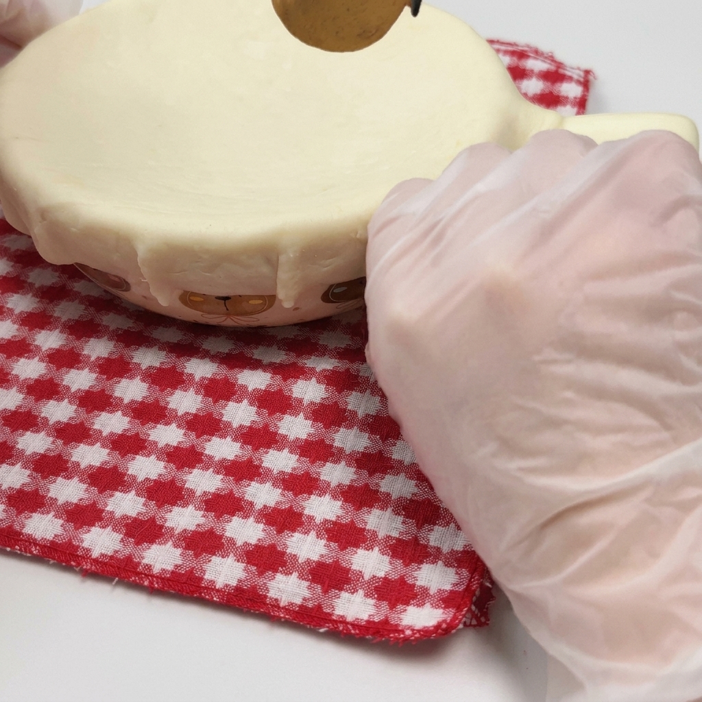 Una mano guantata che preme un foglio di pasta sfoglia sul bordo di una ciotola adatta al forno.