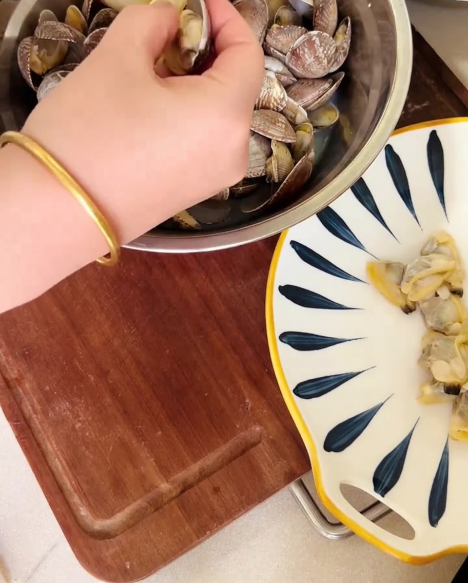 Una mano che estrae i molluschi dai gusci sopra una ciotola, conservando il brodo.